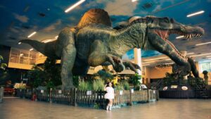 A large dinosaur model in an indoor setting with a child.