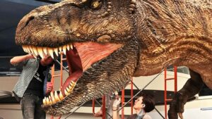 Two people working on a large dinosaur sculpture indoors.