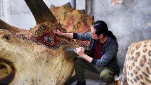 Person working on a detailed dinosaur sculpture in a workshop.