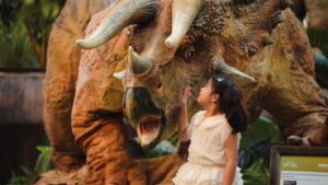 A child interacts with a large dinosaur statue indoors.